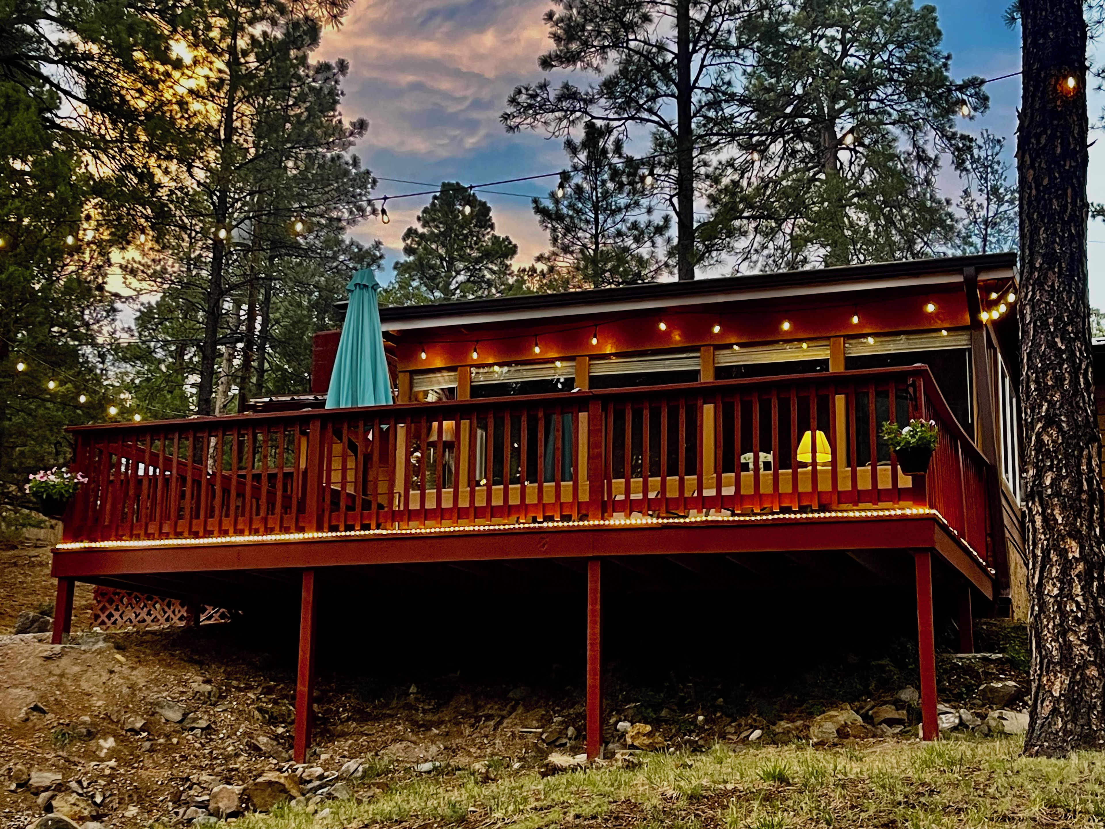 A wooden deck with railings, string lights, and a blue umbrella.