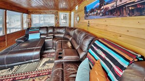 Une pièce chaleureuse, décorée avec des éléments en bois, comprenant un grand canapé en cuir aux lignes arrondies, un tapis à motifs et un téléviseur fixé au mur.