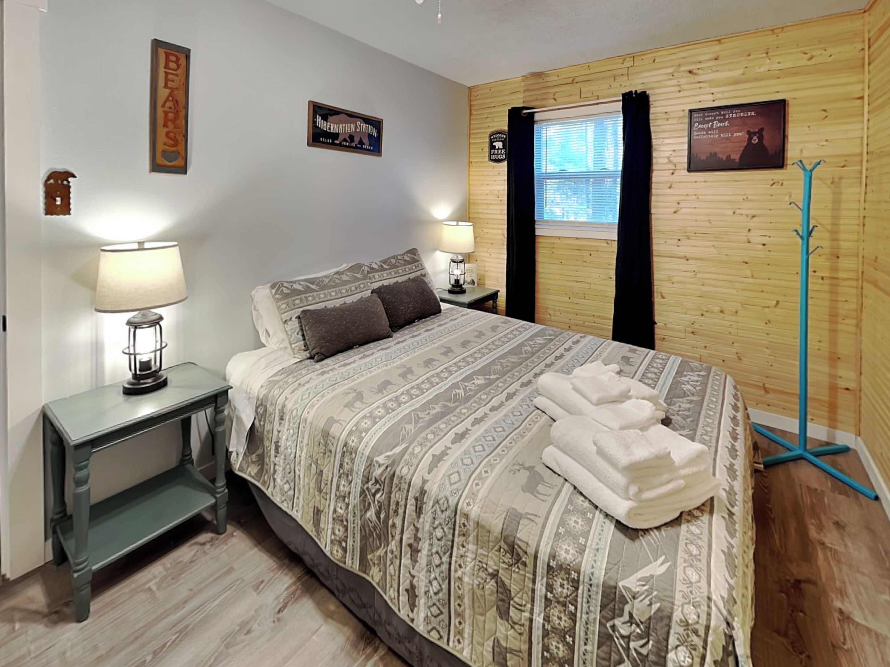 A bedroom with a bed, two bedside tables, a window with curtains, and a coat rack.