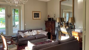 A living room with a sofa, a wooden cabinet, a fireplace, and a chandelier. - Large gîte between Auvergne and Forez heated swimming pool tennis court (Pralong)