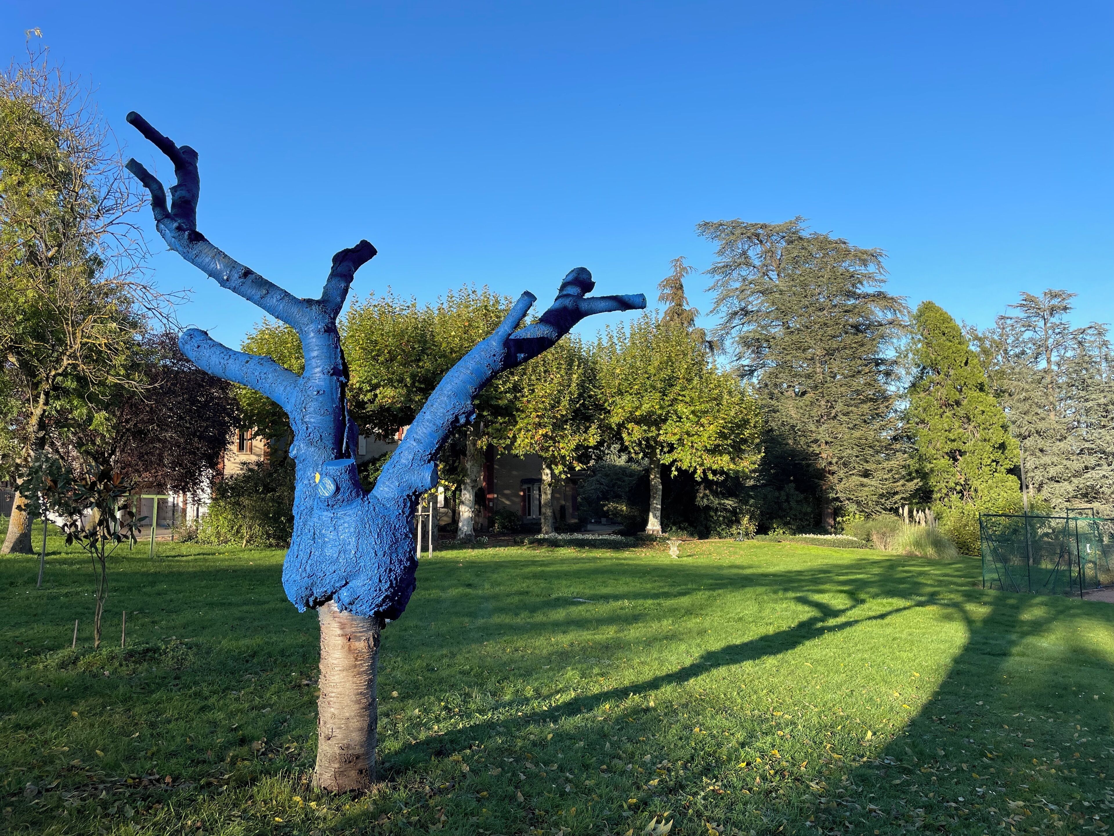 Une sculpture en forme d’arbre au design original, entourée d’une pelouse bien entretenue et de divers arbres en arrière-plan.