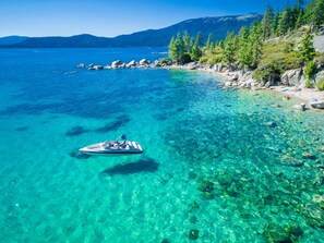 A clear blue lake with a boat, rocky shore, and trees. - 2 Queens | Gondola Views | Rec Center Access | Near Village & Trails (Truckee)