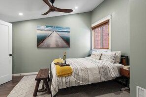 A bedroom with a bed, a desk, a chair, a window, a ceiling fan, and a painting on the wall. - 2 Queens | Gondola Views | Rec Center Access | Near Village & Trails (Truckee)