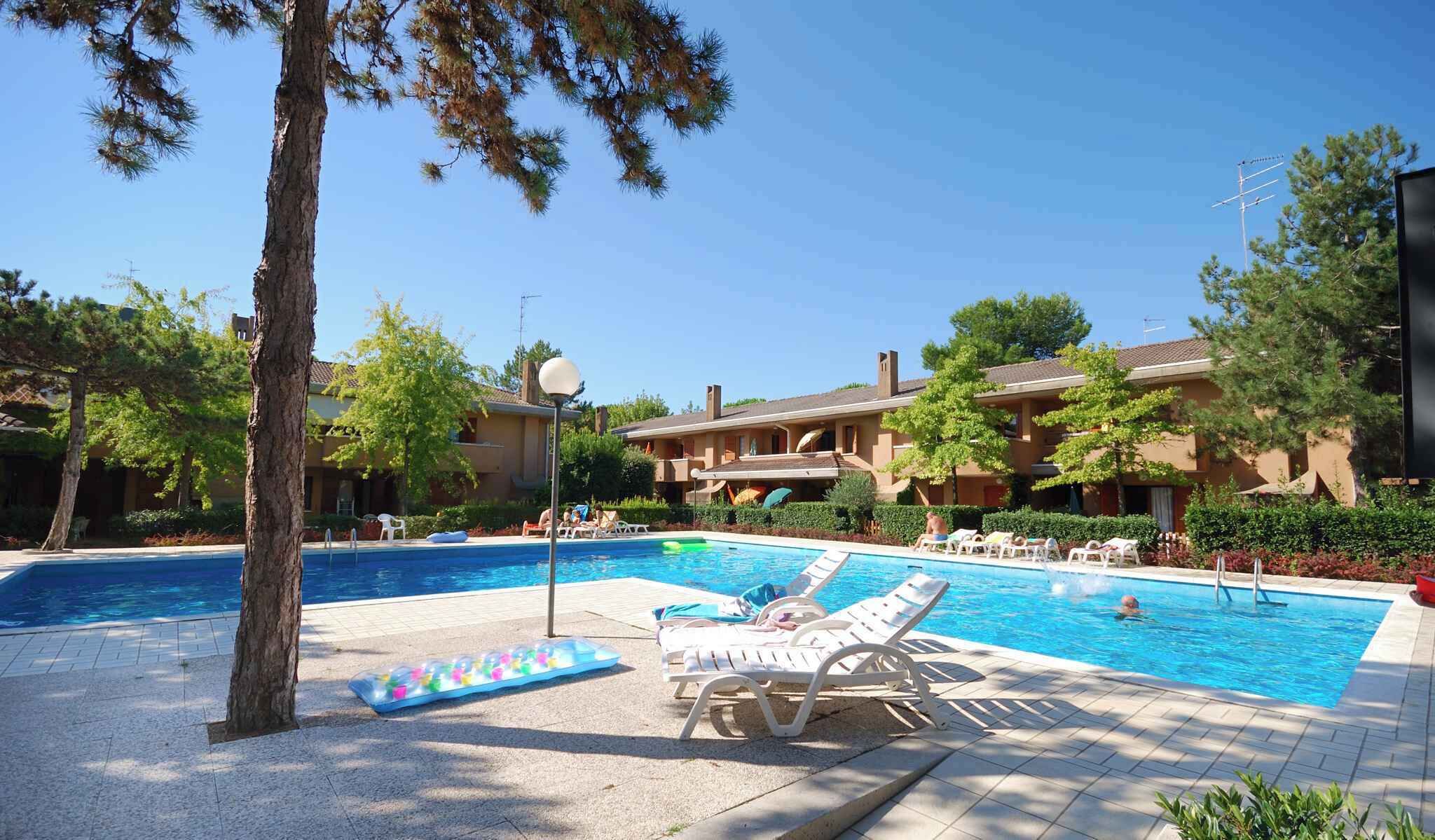 A pool area with lounge chairs, a floating pool noodle, and a building with multiple balconies.