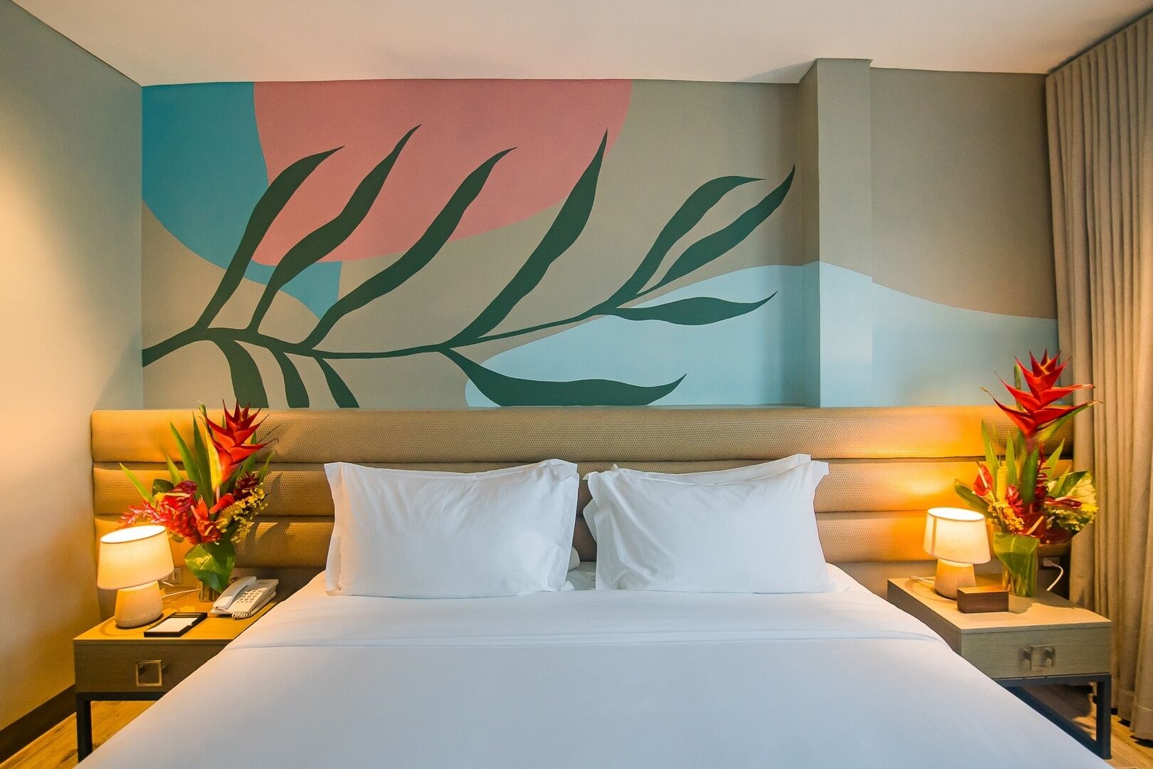 Une chambre d’hôtel avec un lit, deux tables de chevet avec des lampes, un téléphone et un grand tableau abstrait accroché au mur.