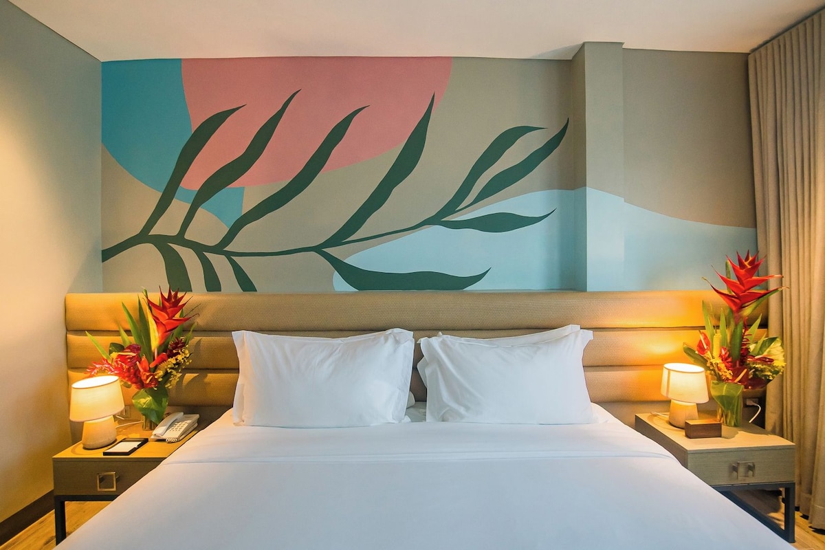 A hotel room with a bed, two bedside tables with lamps, a phone, and a large abstract painting on the wall.