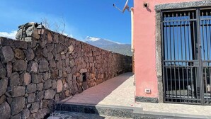 Un muro de piedra, un edificio rosa con una reja negra, y un cielo azul despejado.