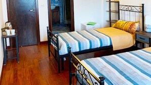 Un dormitorio con dos camas, suelo de madera, un armario, una mesita de noche y una estantería en la pared.