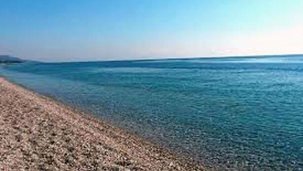 Una playa con agua cristalina y orilla pedregosa.