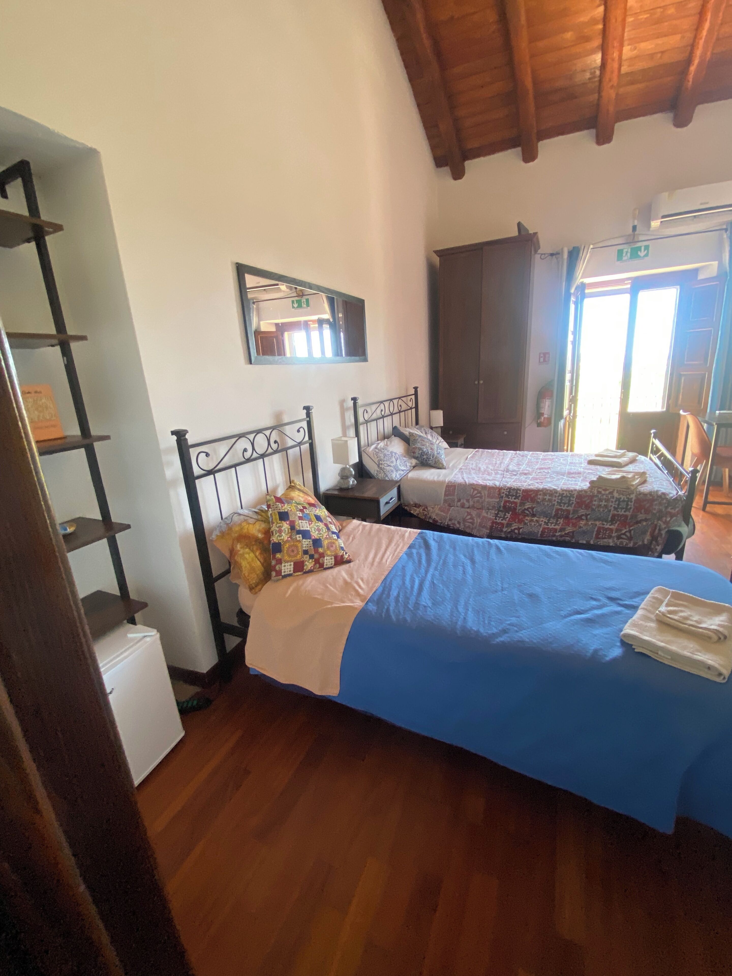 Un dormitorio con dos camas, techo de madera, pared blanca y una ventana.