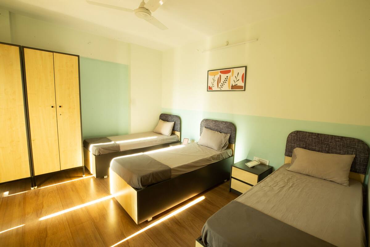 A hotel room with two single beds, a wardrobe, a nightstand, and a ceiling fan.