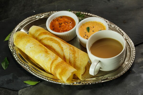 A plate with two rolled crepes, two small bowls of chutney, and a cup of tea.