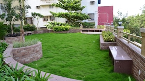 Un jardin bien entretenu, avec une pelouse soigneusement taillée, des jardinières en briques et une variété d’arbustes et d’arbres.