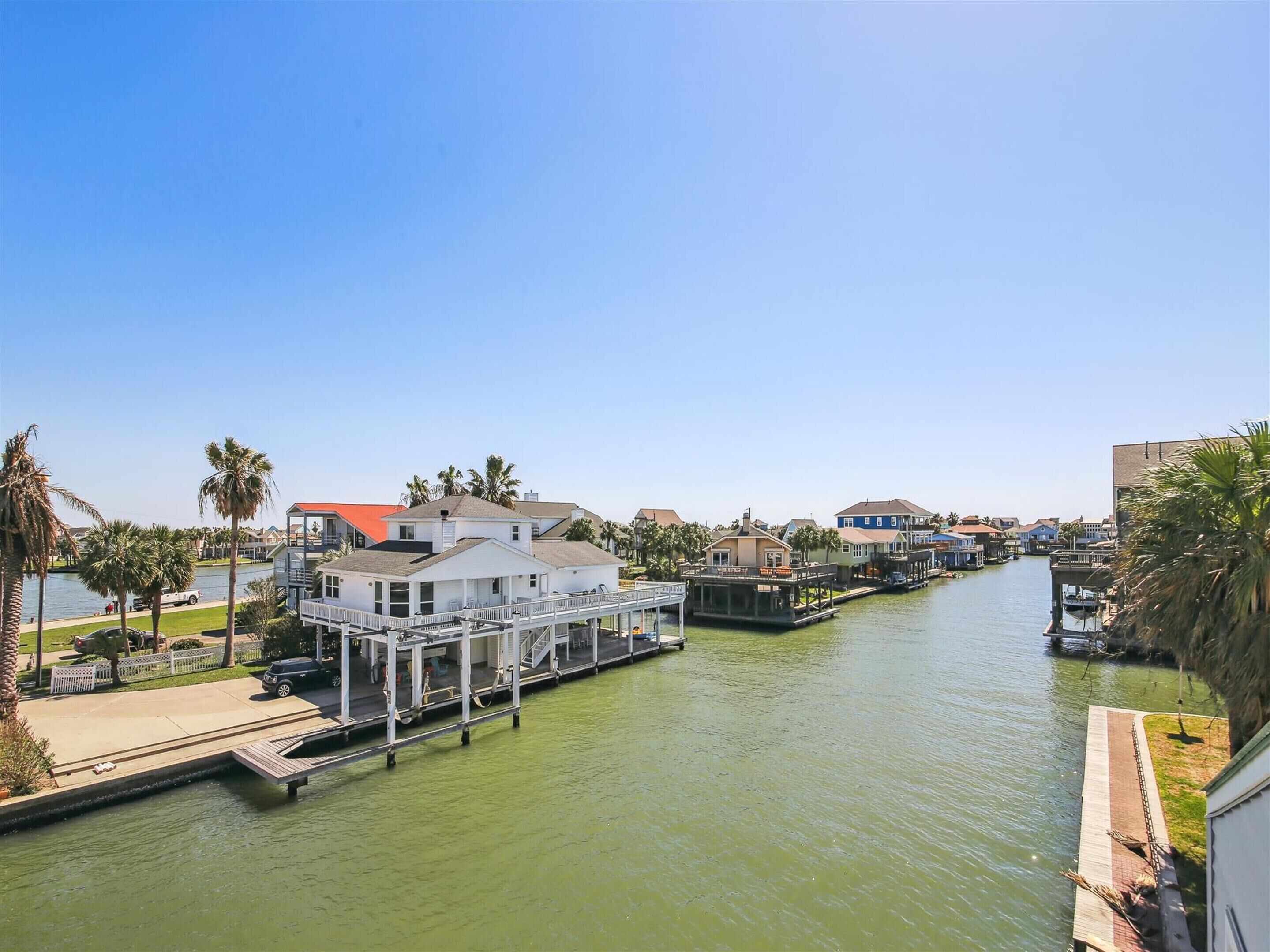 Un canal con un muelle, casas y palmeras.