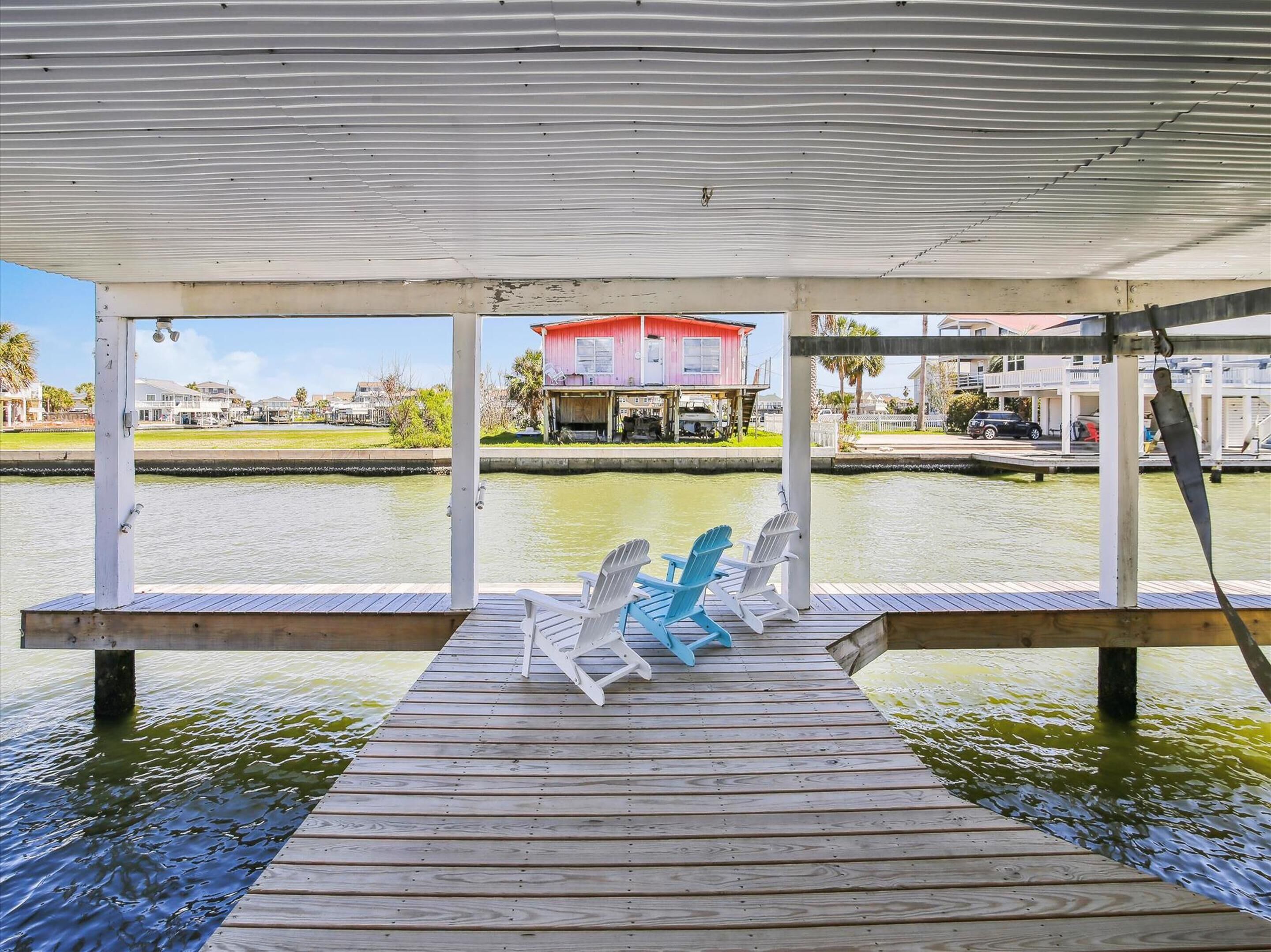 A wooden dock with two white Adirondack chairs facing a body of water.