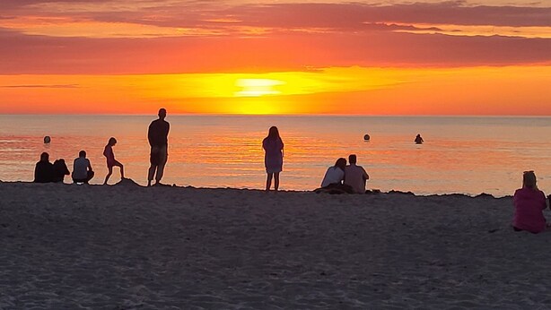 A beach scene with people sitting and standing, facing the sunset. - Ferienwohnung Nähe Ostsee (Ribnitz-Damgarten)