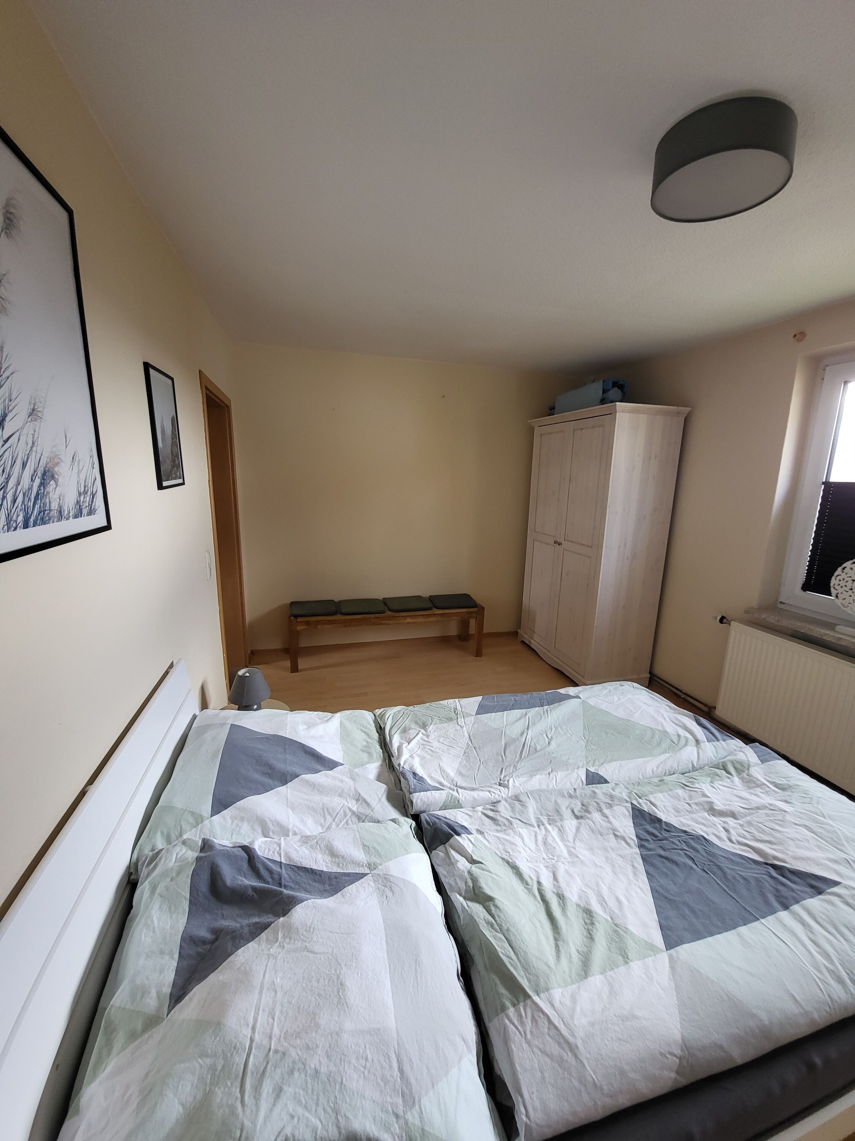 Un dormitorio con cama, un banco, un armario y cuadros en la pared.