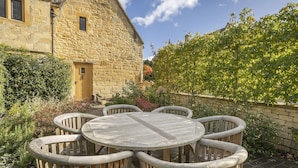 A stone building with a wooden door and a round table with six chairs.