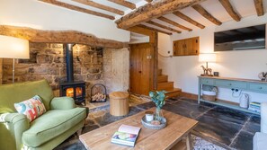 Ein gemütliches Wohnzimmer mit Kamin aus Stein, einem grünen Sofa, einem Holztisch und einer Treppe, die zu einer Holztür führt.