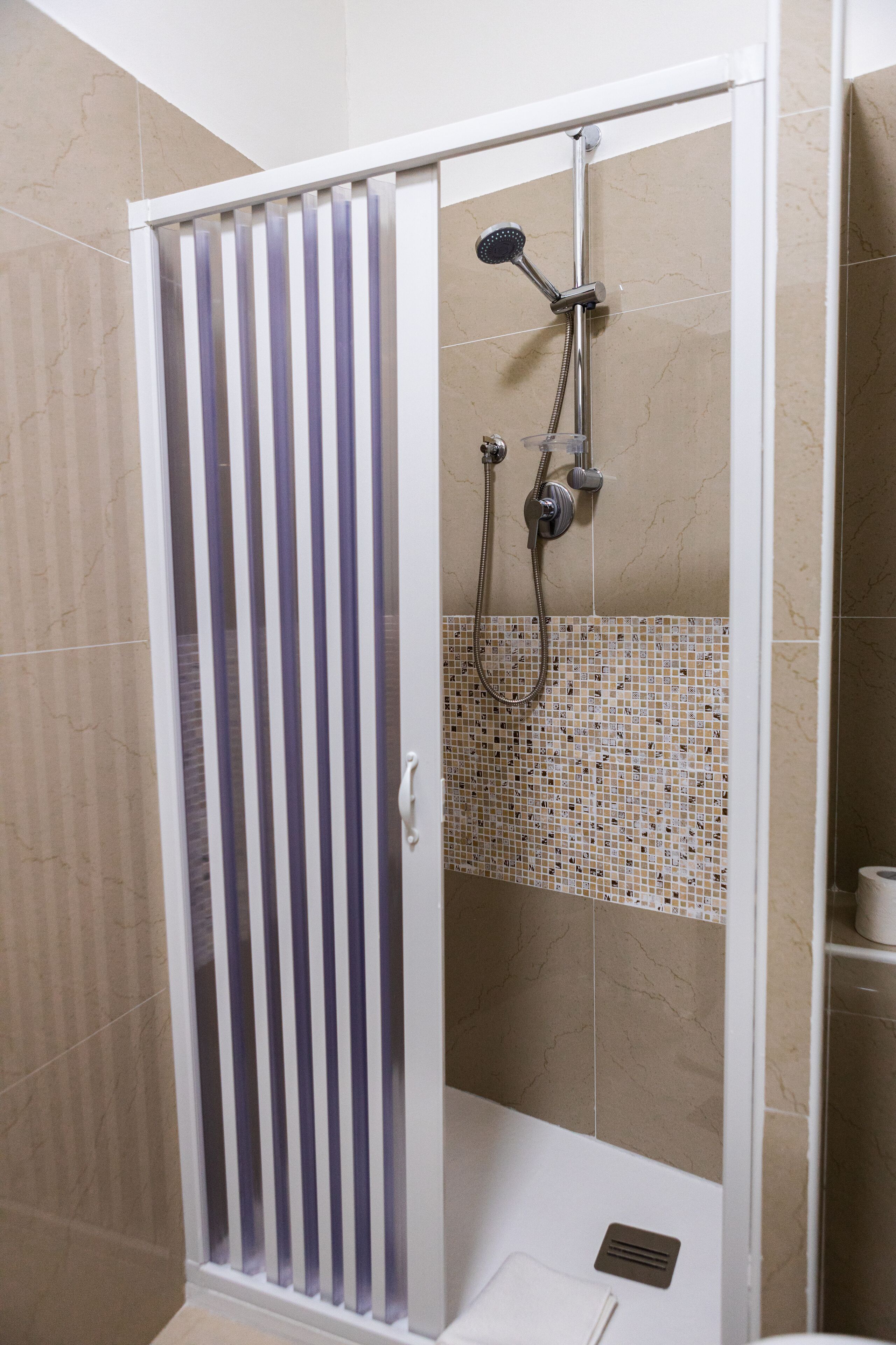 A shower enclosure with a glass door, a handheld showerhead, and a wall-mounted faucet.