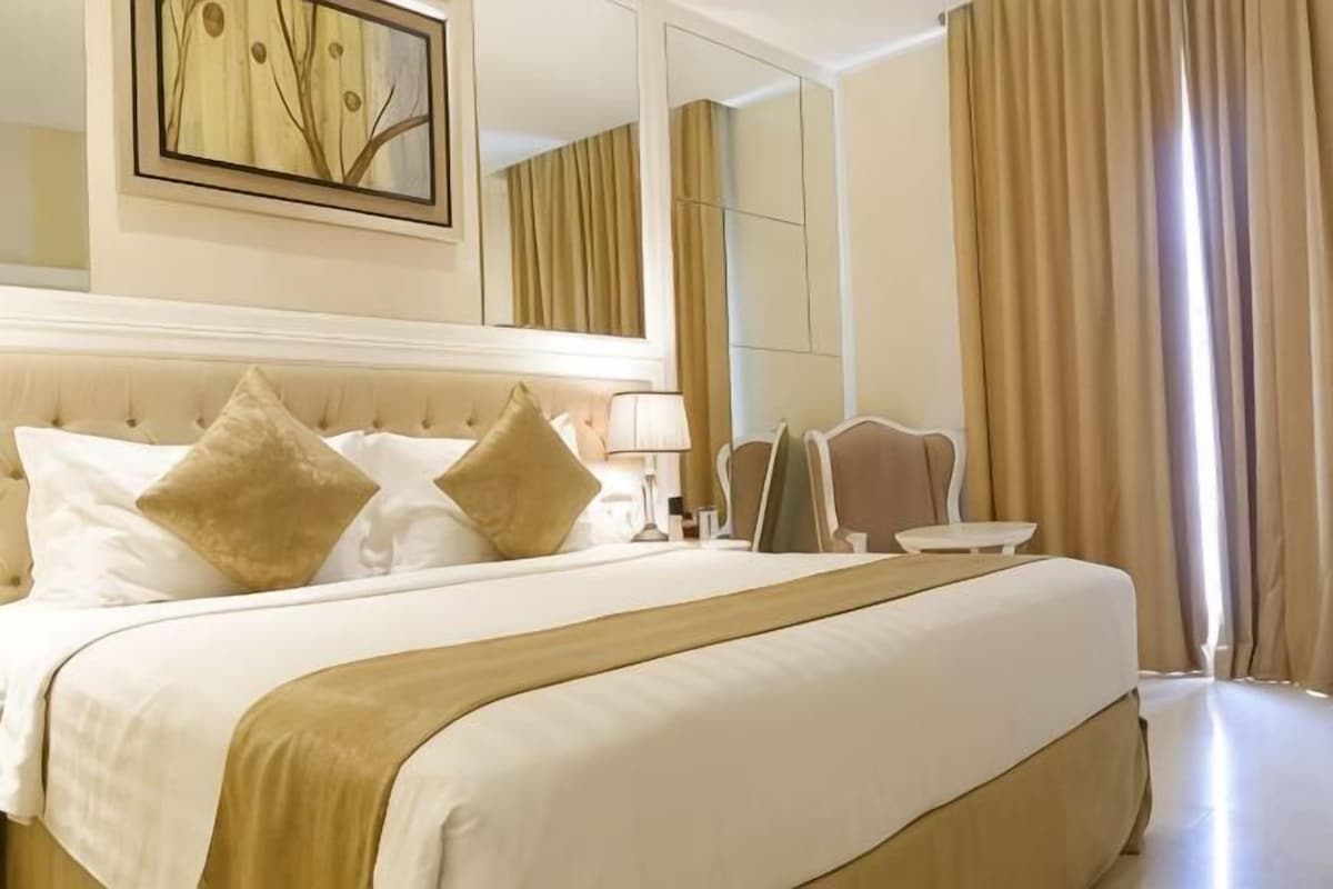 A hotel room with a large bed, a mirror, a bedside table, and a view of the outside.