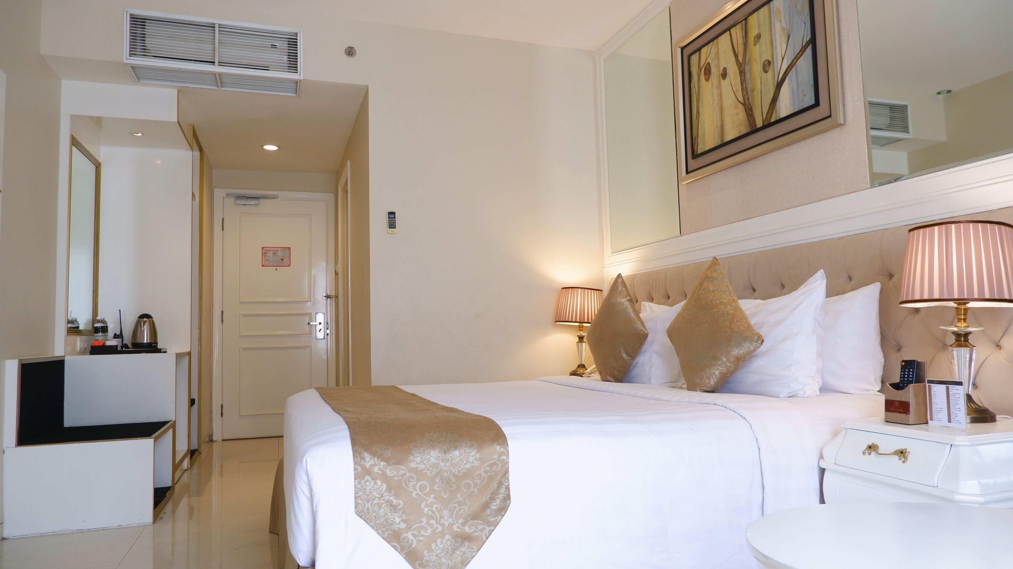 Een hotelkamer met een bed, bedlampjes, een nachtkastje, een spiegel en een deur.