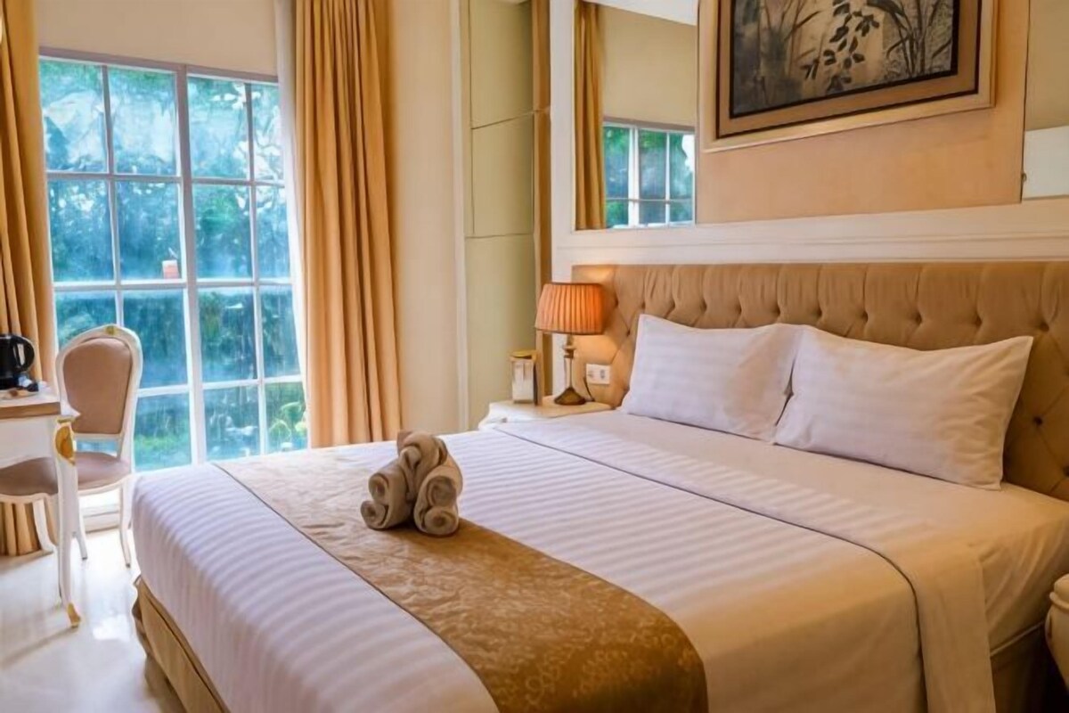 A hotel room with a large bed, a desk, a chair, and a window with curtains.