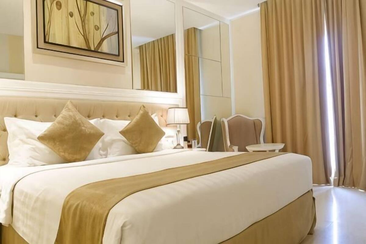 Habitación de hotel con una cama grande, un espejo, una mesita de noche y vistas al exterior.
