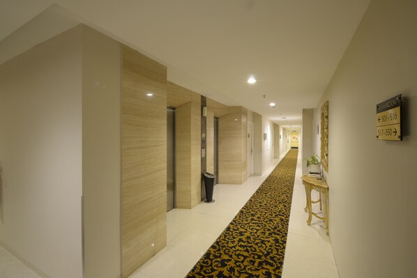 Un couloir d’hôtel avec un tapis à motifs, un comptoir de réception et des panneaux d’orientation.