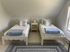 Two single beds with white bedspreads and blue throw blankets, a bedside table, and a patterned rug.