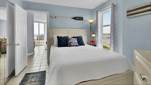 Een slaapkamer met een bed, nachtkastje, lamp en uitzicht op het strand.
