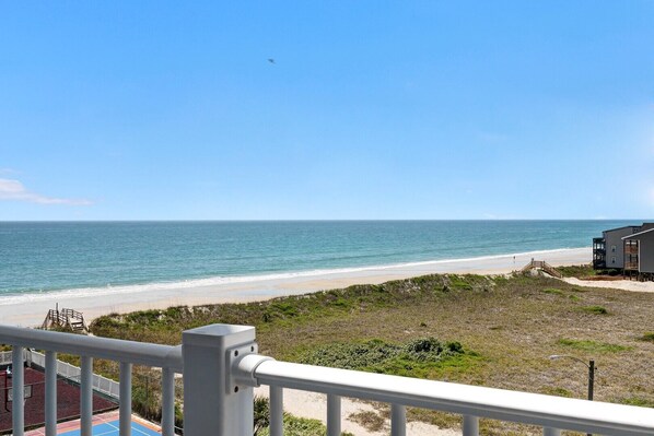 A beachfront property with a view of the ocean, a wooden deck, and a building with balconies.