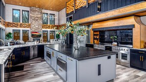 A spacious kitchen with a large island, built-in appliances, and a high ceiling with wooden beams.