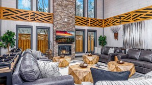 A modern living room with a fireplace, leather sofas, wooden coffee tables, and large windows.