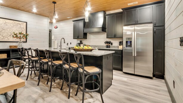 Una cocina moderna con armarios oscuros, electrodomésticos de acero inoxidable y una isla central con taburetes de bar.