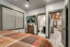 A bedroom with a large bed, a dresser, and a painting on the wall. There is a bathroom visible through an open door.