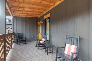 Relax in a serene outdoor space with a wooden deck, three comfortable rocking chairs, and a small table.
