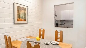 En matplats med en vit tegelvägg, en inramad tavla som föreställer en skog och utsikt över ett kök genom ett fönster.
