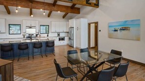 Een moderne keuken met witte kasten, een centraal eiland met barkrukken, en een eethoek met een glazen tafel en stoelen.