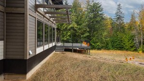 Een modern huis met grote ramen, een terras en een bebost achtergrond.