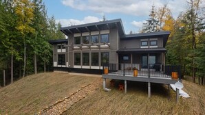 Een modern huis met twee verdiepingen en een terras, omringd door bebossing.