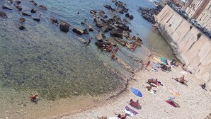 Una playa con aguas cristalinas, costa rocosa y gente tomando el sol.