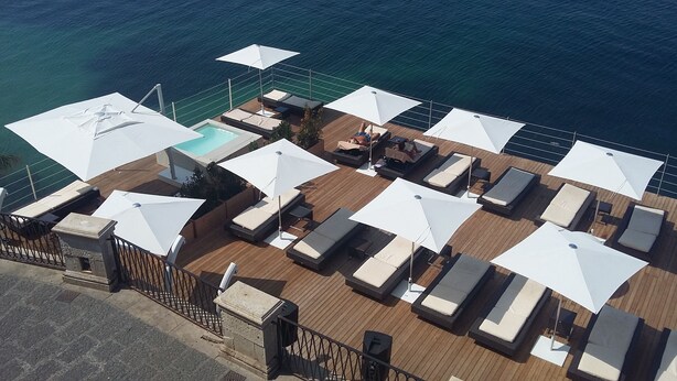 Vista aérea de una terraza con múltiples tumbonas, una piscina y sombrillas.