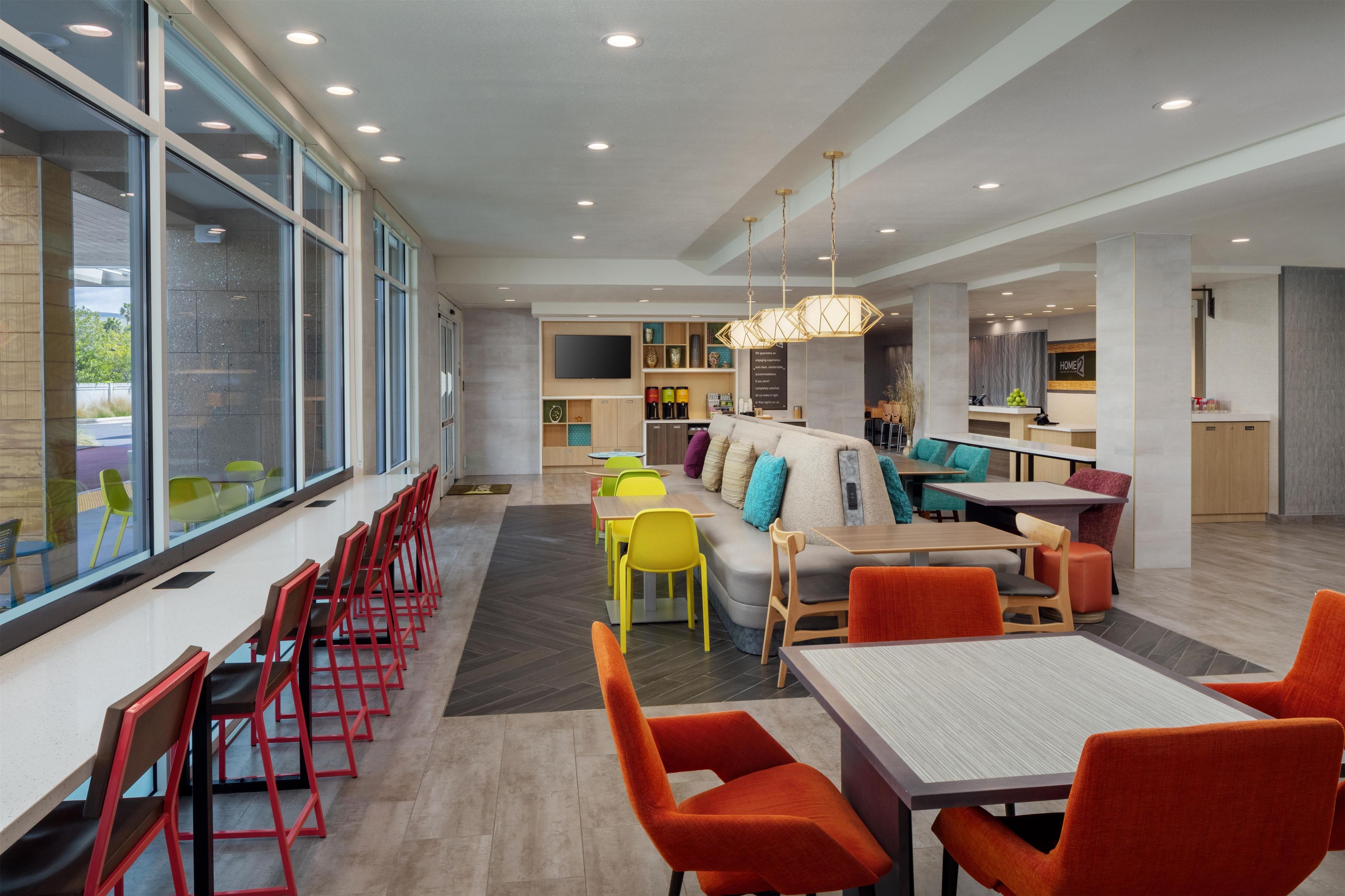 A modern hotel lobby with a long reception desk, seating area with colorful chairs, a sofa, and a large window offering a view.