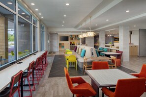 Een moderne hotel lobby met een lange receptiebalie, een zithoek met kleurrijke stoelen, een bank en een groot raam met uitzicht.