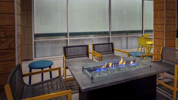 Een moderne buitenruimte met een vuurplaats met glazen blad, rieten stoelen en uitzicht door glasverfde ramen.