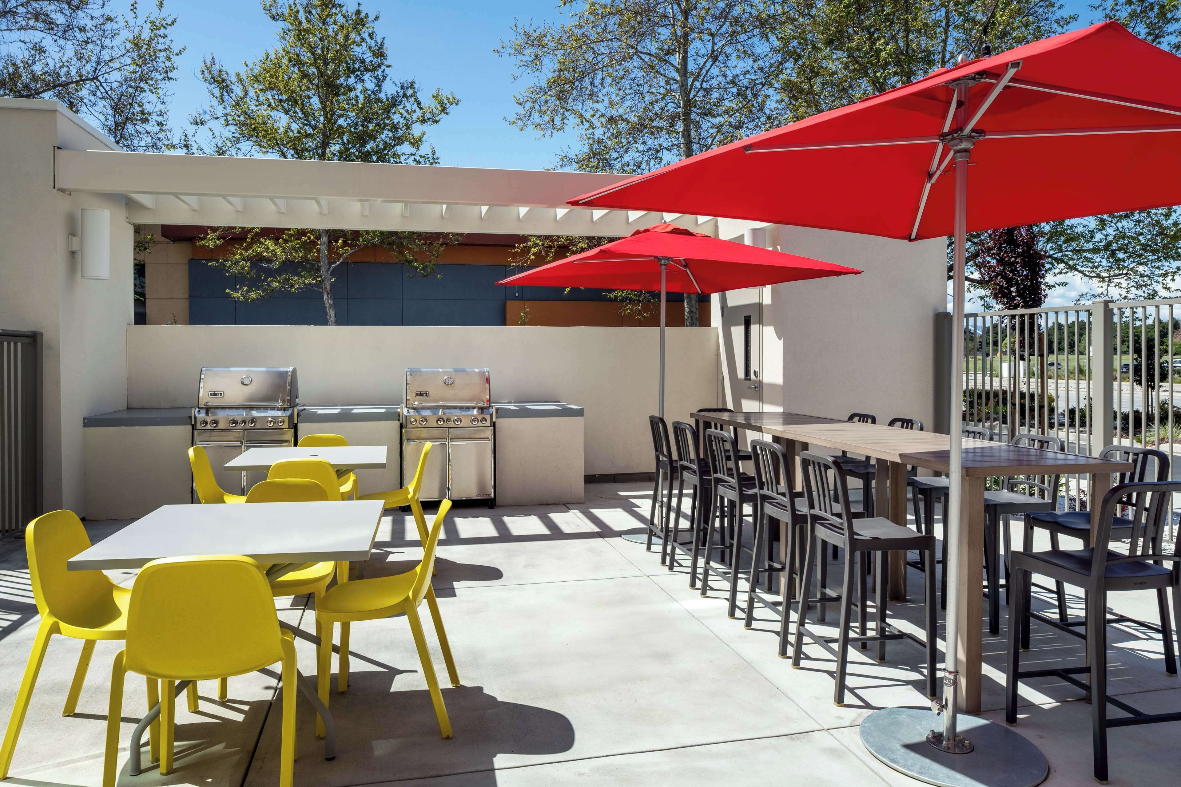 An outdoor patio with yellow and black chairs, a red umbrella, and a grill area.