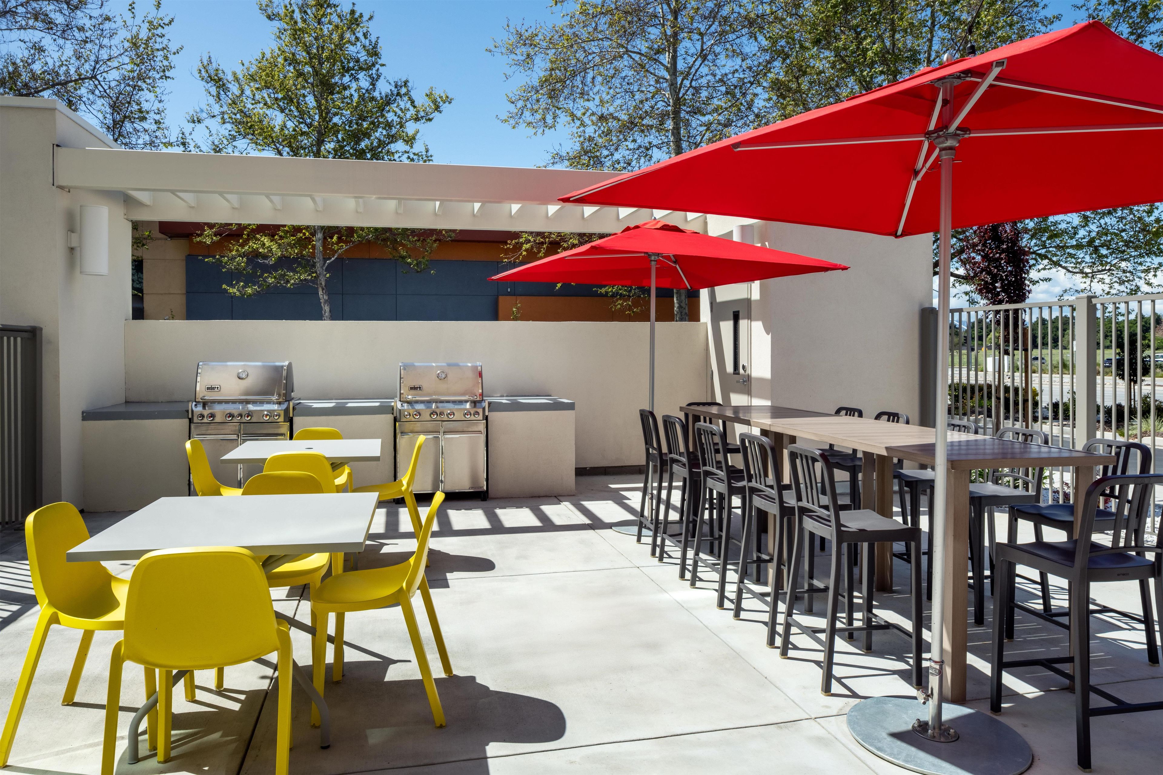 An outdoor patio with yellow chairs, a grill, and red umbrellas.