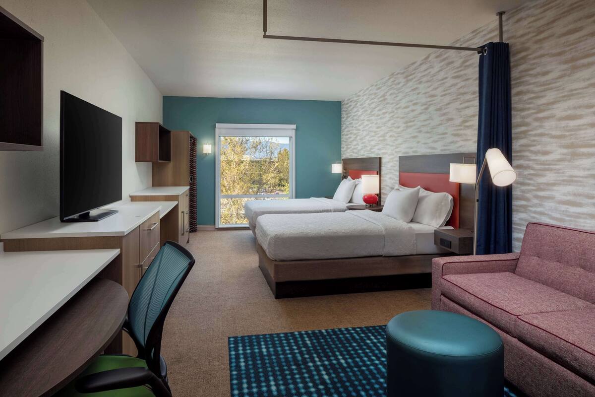 Ein Hotelzimmer mit einem Bett, zwei Nachttischen, einem Schreibtisch mit Stuhl, einem Fernseher und einem Sofa.