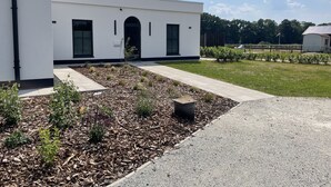 En moderne bygning med en lys, hvid facade, en lille indgang og en velholdt have med barkdække og beplantning.